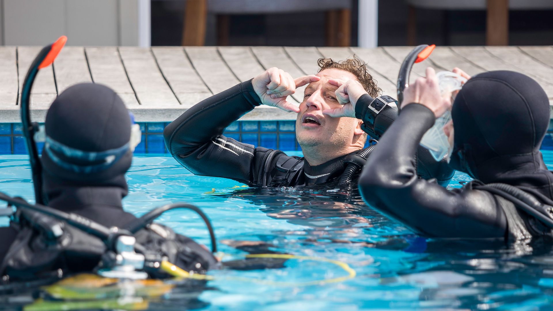 Duiker oefent het leegmaken van zijn duikmasker tijdens een zwembadtraining