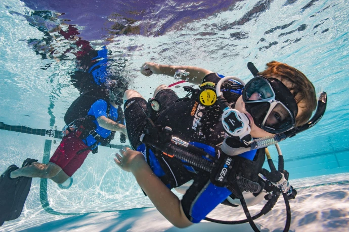 Groep cursisten oefent op de bodem van het zwembad met hun instructeur