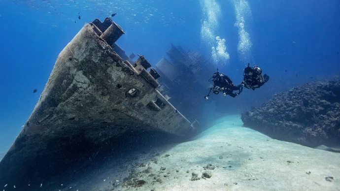 Duikers verkennen een scheepswrak op zandbodem tijdens de PADI Wreck Diver